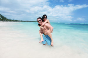 Pareja feliz y juguetona divirtiéndose en un tramo desierto de la hermosa playa caribeña.