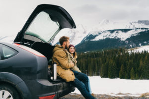 Young Caucasian couple resting near the car in mountains in winter
