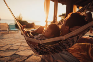 Photo of a little boy and his father having a relaxing moment in a hammock on a terrace of their family home by the sea