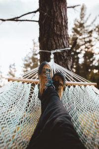 Crop shot of female feet relaxing in hammock among coniferous trees.