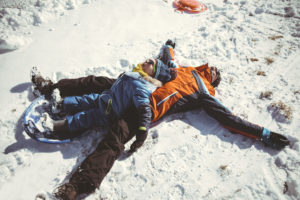 Italy, Val Venosta, Slingia, happy father and son lying in snow